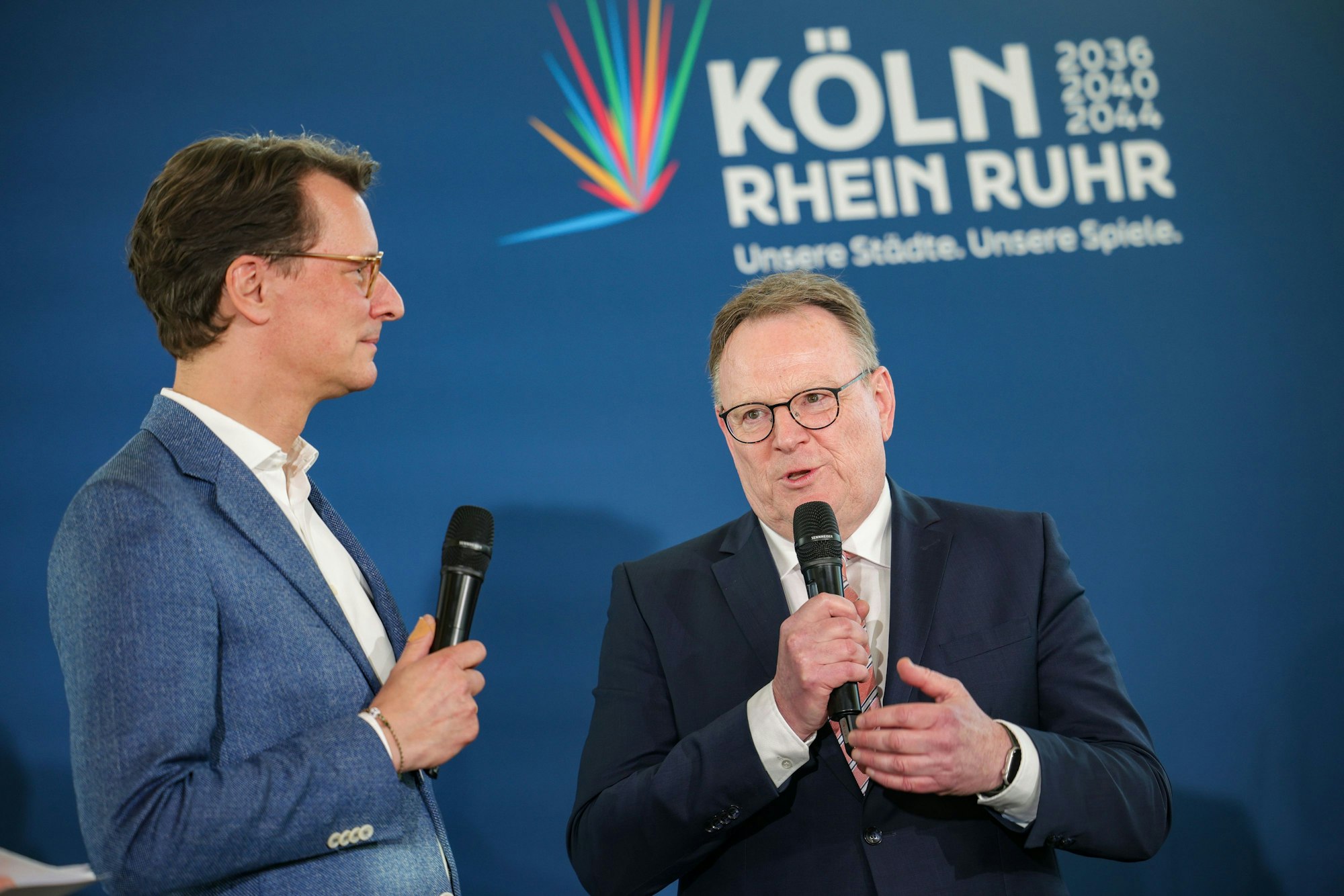 Hendrik Wüst (CDU, l-r), Ministerpräsident des Landes NRW, und Torsten Burmester (SPD), Oberbürgermeister der Stadt Köln sprechen auf der Bühne am Wahlabend in Köln.