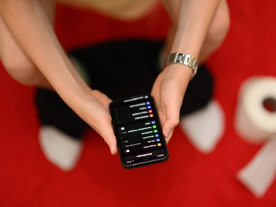 Ein junger Mann sitzt mit einem Handy auf einer Toilette