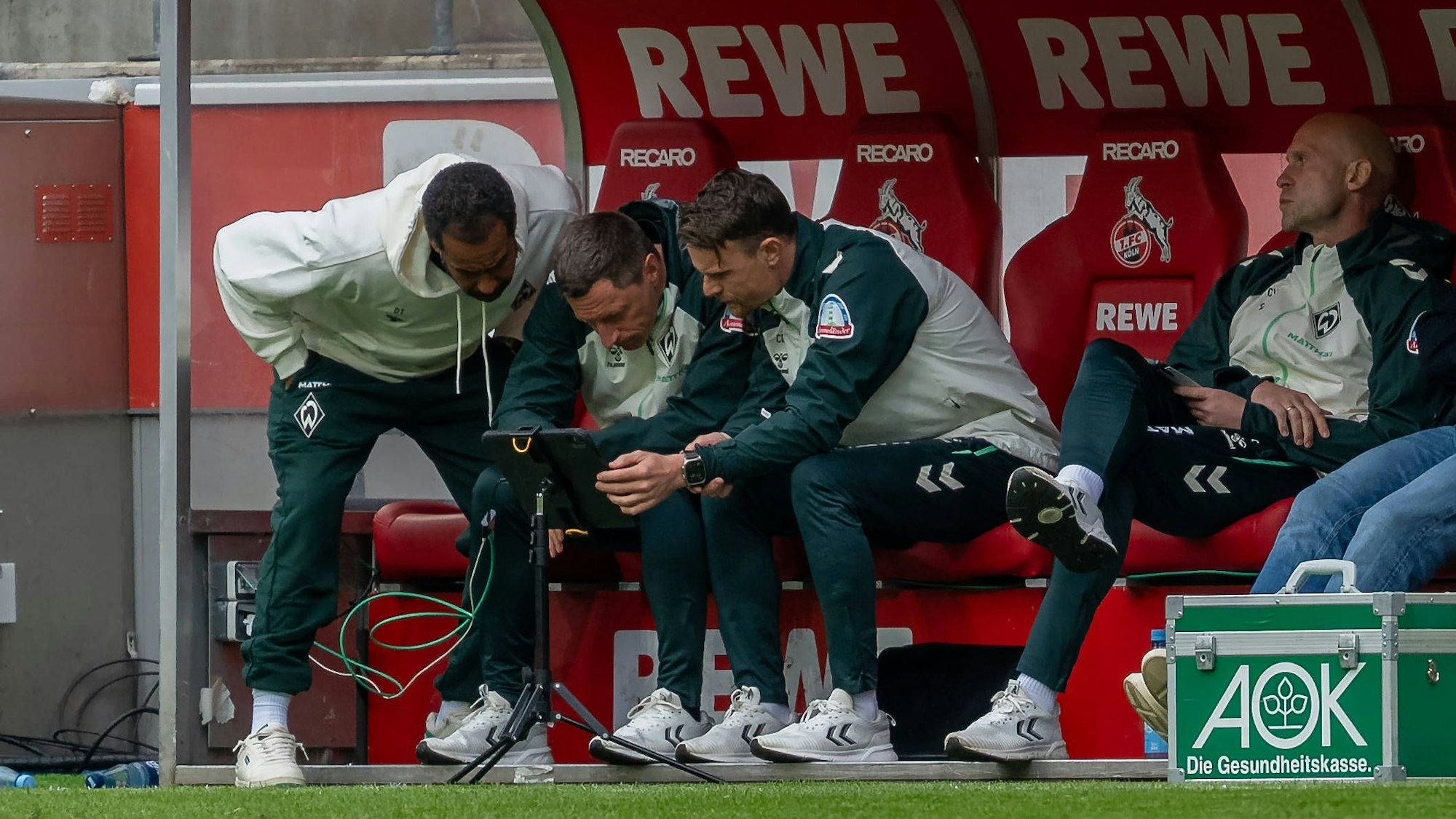 Das Trainerteam von Werder Bremen schaut während des Spiels auf ein Tablet.