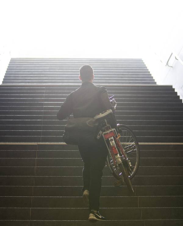 Mann trägt sein Fahrrad eine Treppe hinauf