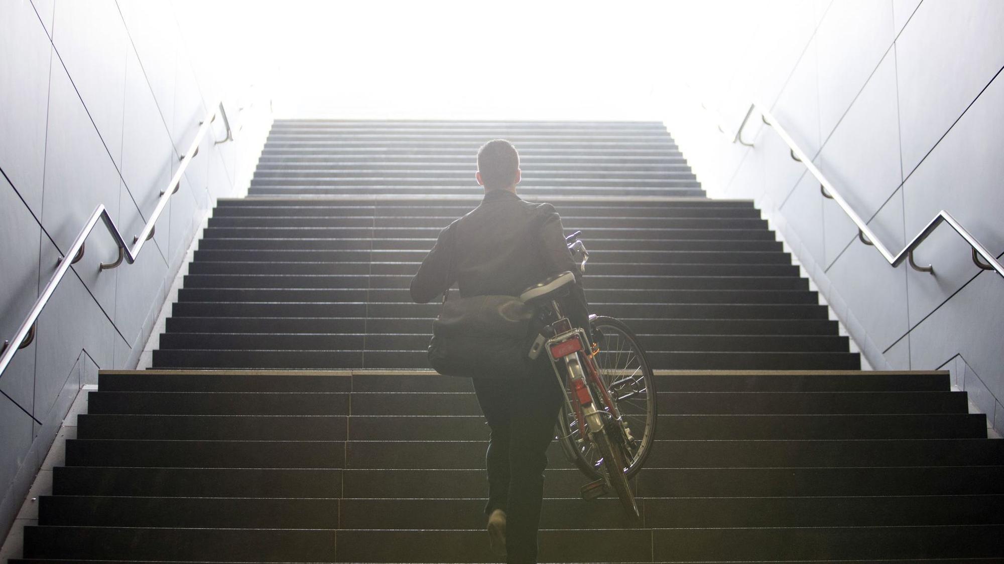 Mann trägt sein Fahrrad eine Treppe hinauf