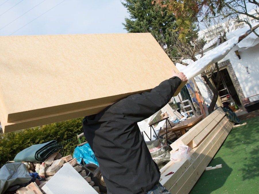 Arbeiter trägt Dämmplatten auf eine Baustelle