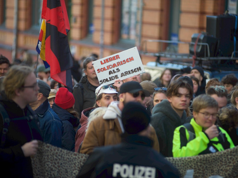 Menschenmenge bei Demonstration mit Plakat und Polizist