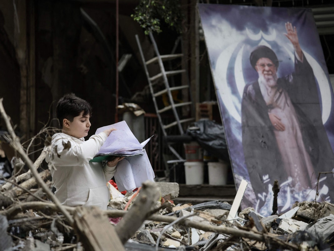 Ein Junge steht inmitten der Trümmer eines Gebäudes neben einem Porträt des getöteten Iran-Führers Ayatollah Ali Khamenei.