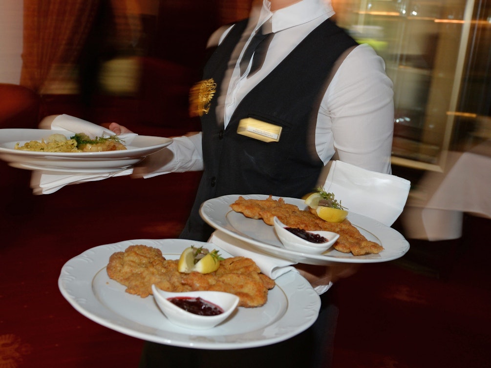 Eine Bedienung serviert in einem Restaurant Teller mit Schnitzeln.