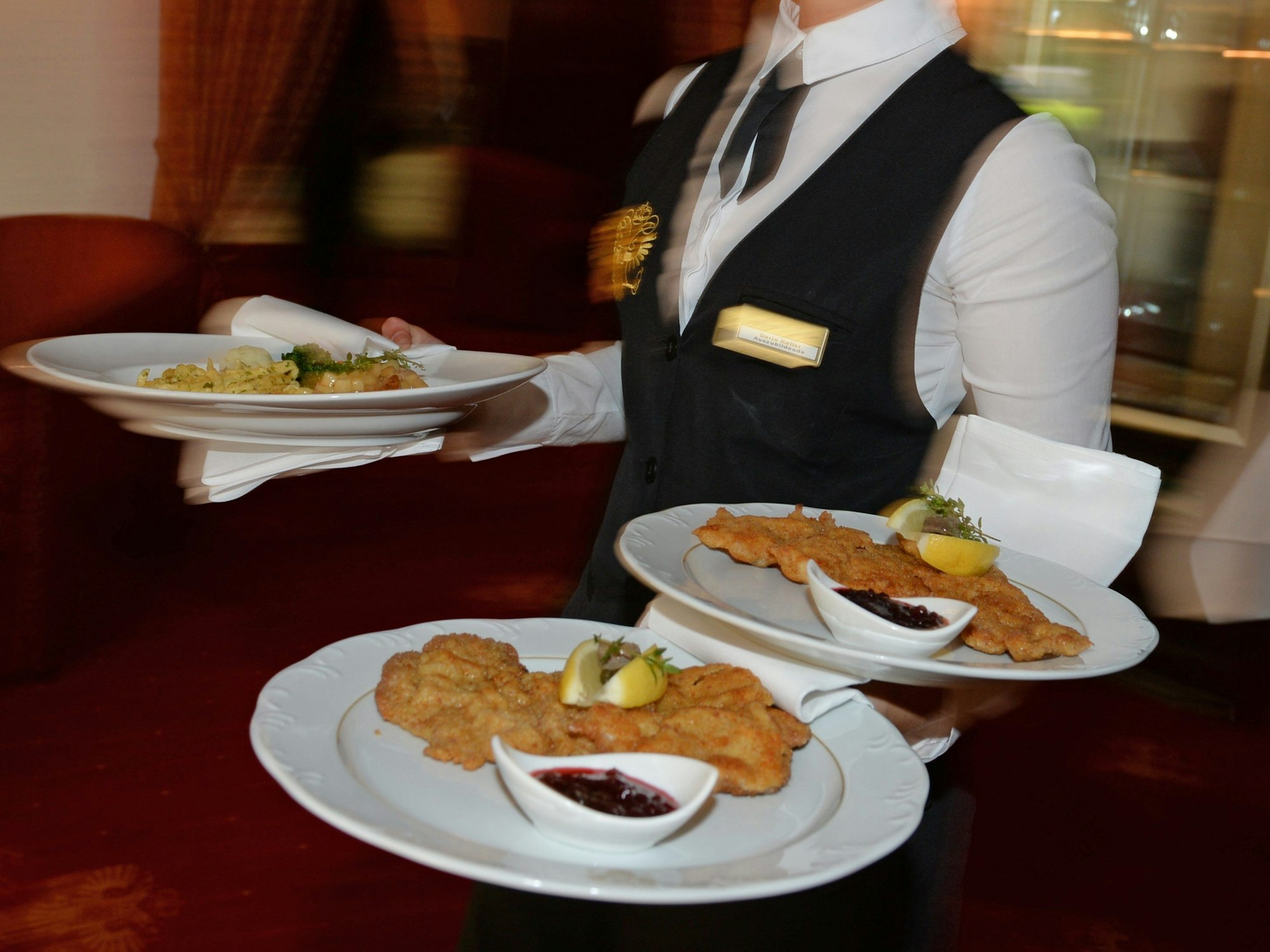 Eine Bedienung serviert in einem Restaurant Teller mit Schnitzeln.