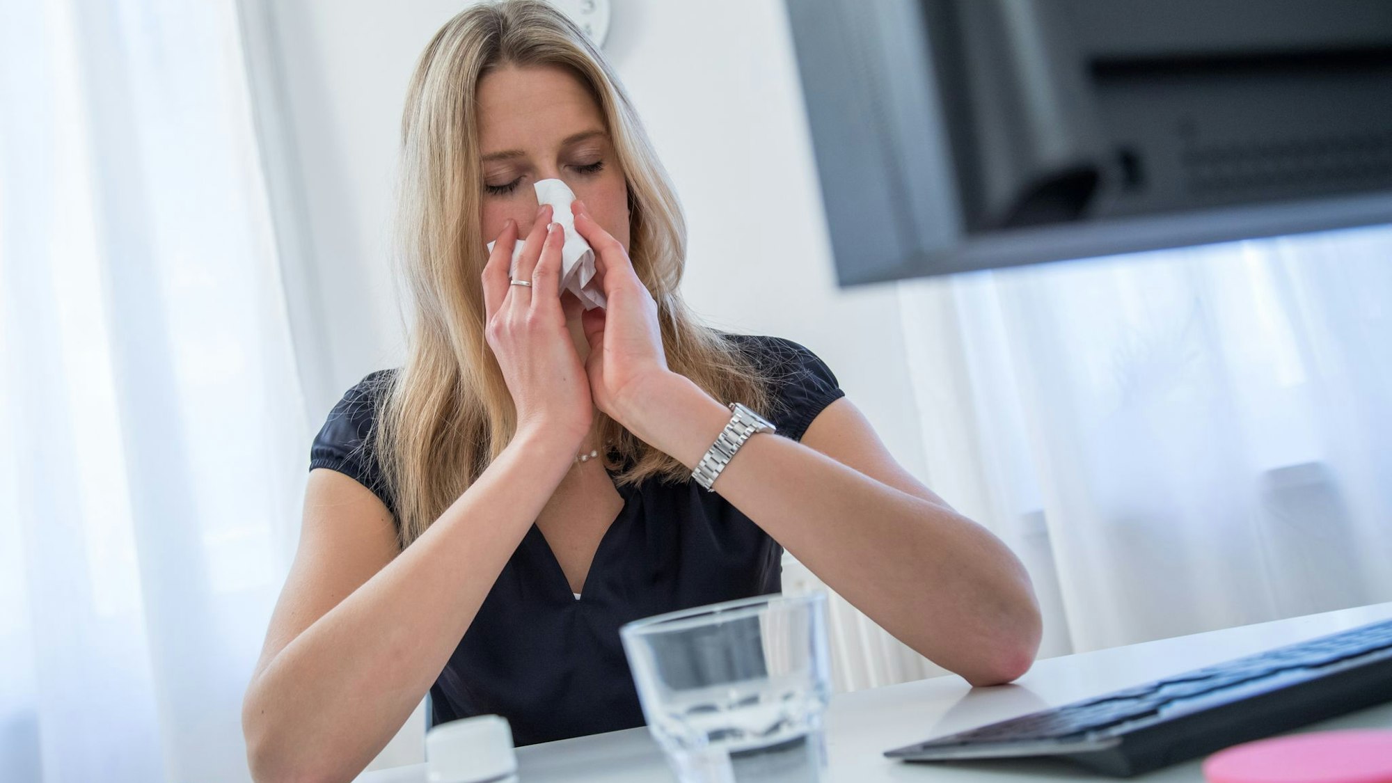 Frau sitzt erkältet vor ihrem Rechner zu Hause