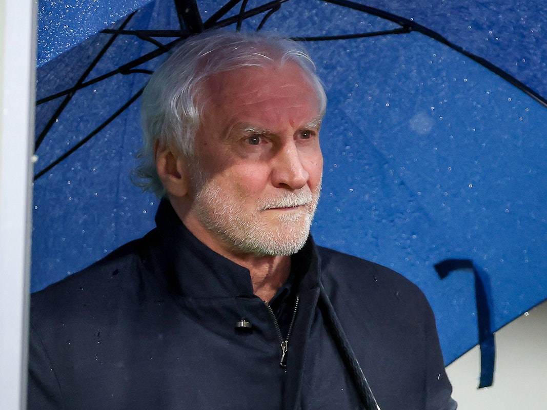 Sportdirektor Rudi Völler hält einen blauen Regenschirm in der Hand.