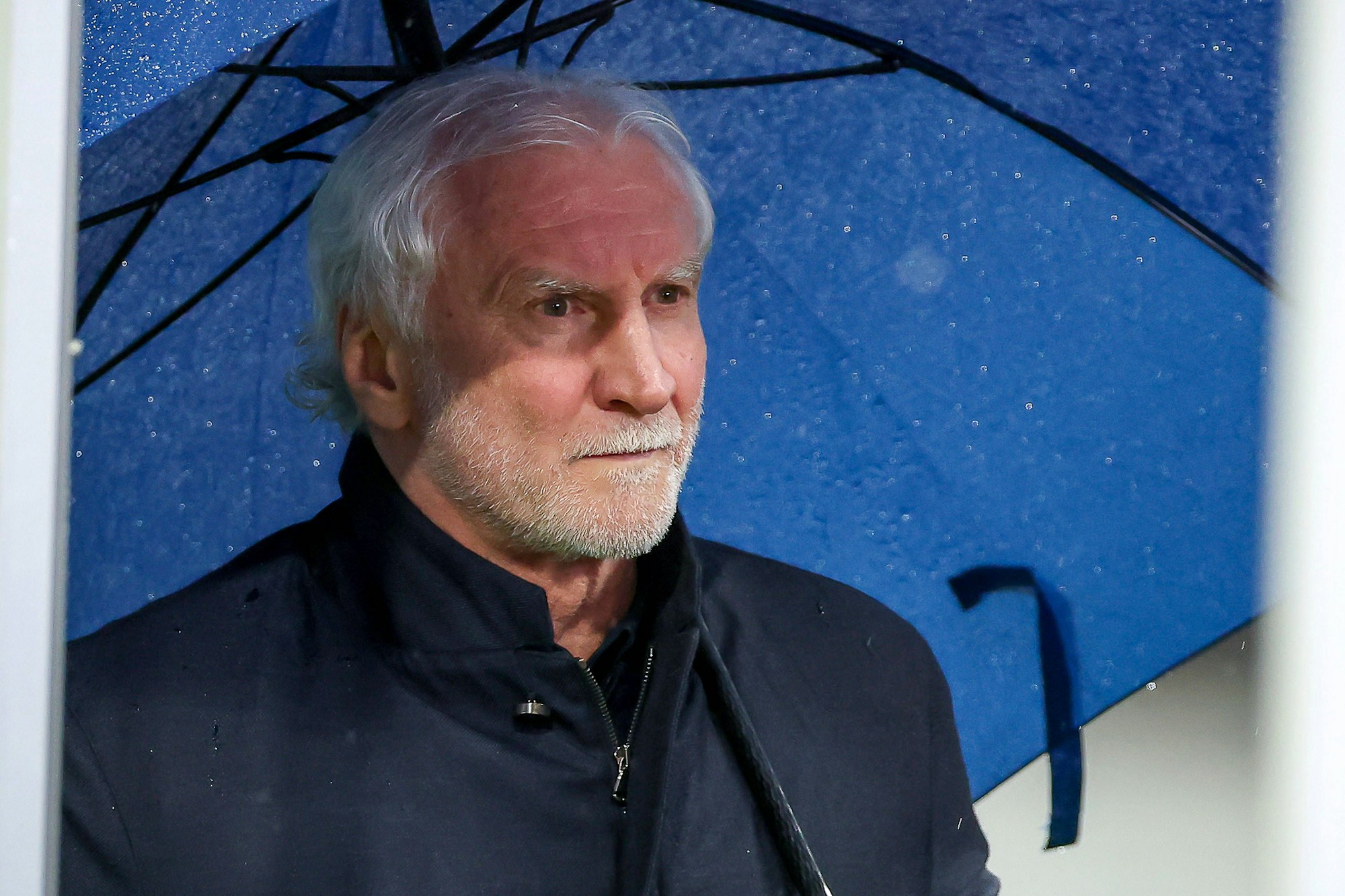 Sportdirektor Rudi Völler hält einen blauen Regenschirm in der Hand.