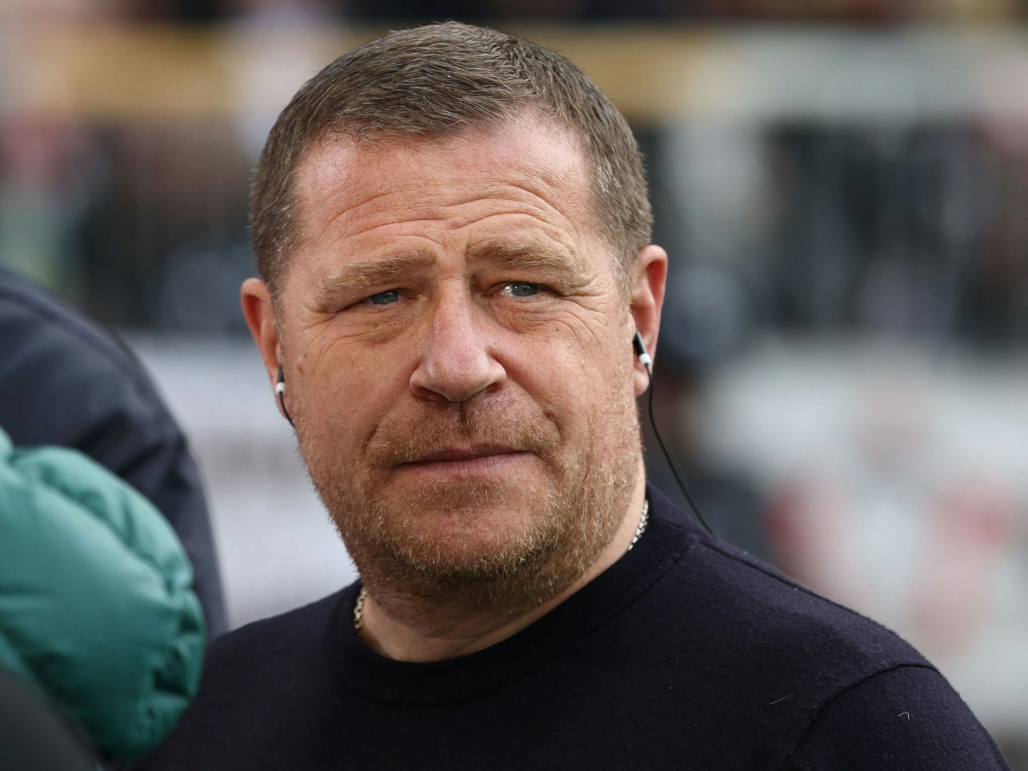 Sportboss Max Eberl trägt vor dem Spiel bei einem Interview Kopfhörer im Ohr.