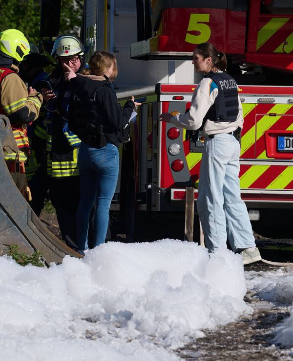 Einsatzkräfte der Polizei, der Feuerwehr und ein Fahrzeug der Feuerwehr sind hinter Löschschaum zu sehen. In Dortmund war in einem leerstehenden Gebäude ein Feuer ausgebrochen.