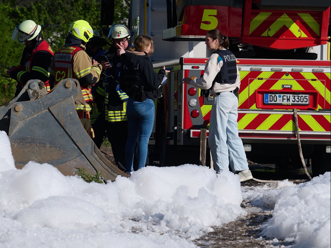 Einsatzkräfte der Polizei, der Feuerwehr und ein Fahrzeug der Feuerwehr sind hinter Löschschaum zu sehen. In Dortmund war in einem leerstehenden Gebäude ein Feuer ausgebrochen.