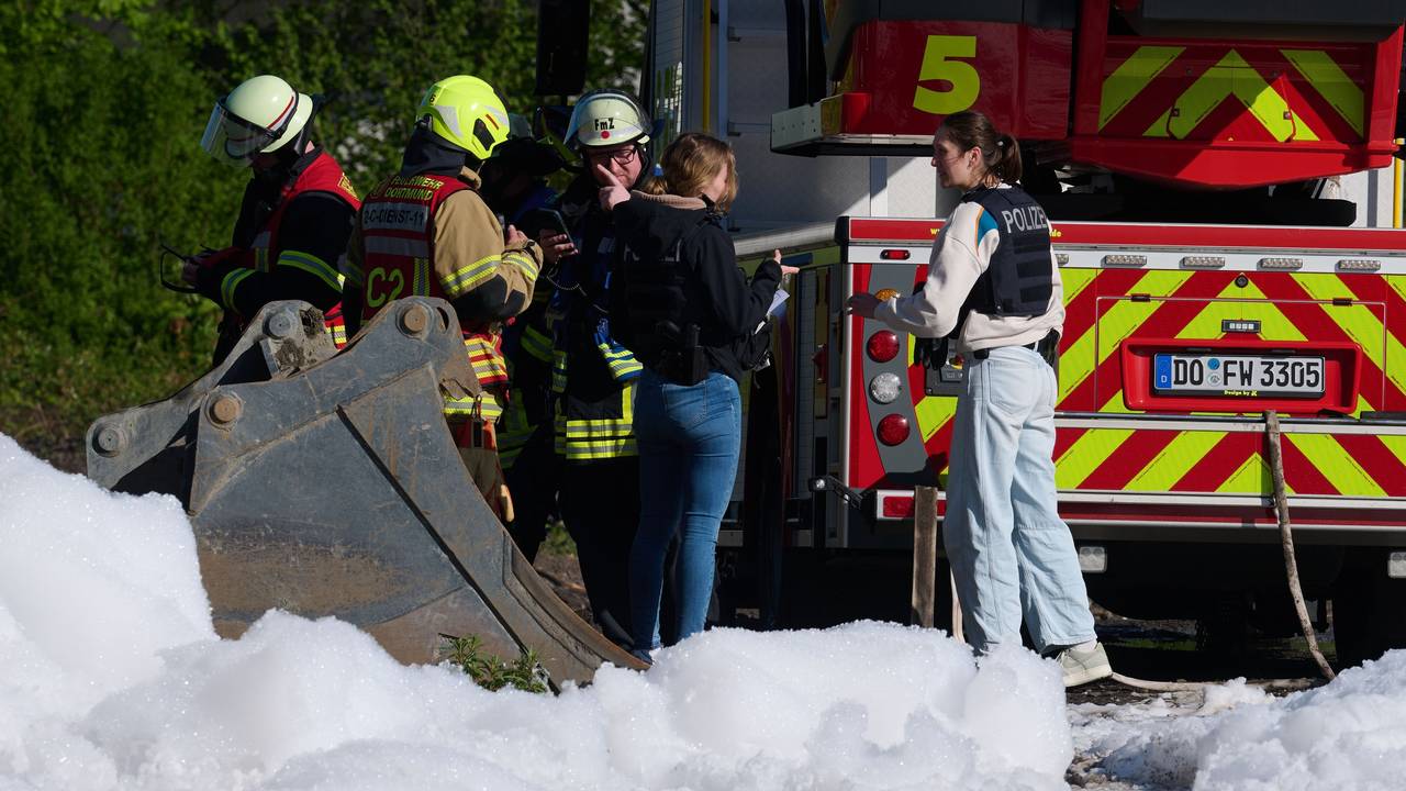 Einsatzkräfte der Polizei, der Feuerwehr und ein Fahrzeug der Feuerwehr sind hinter Löschschaum zu sehen. In Dortmund war in einem leerstehenden Gebäude ein Feuer ausgebrochen.