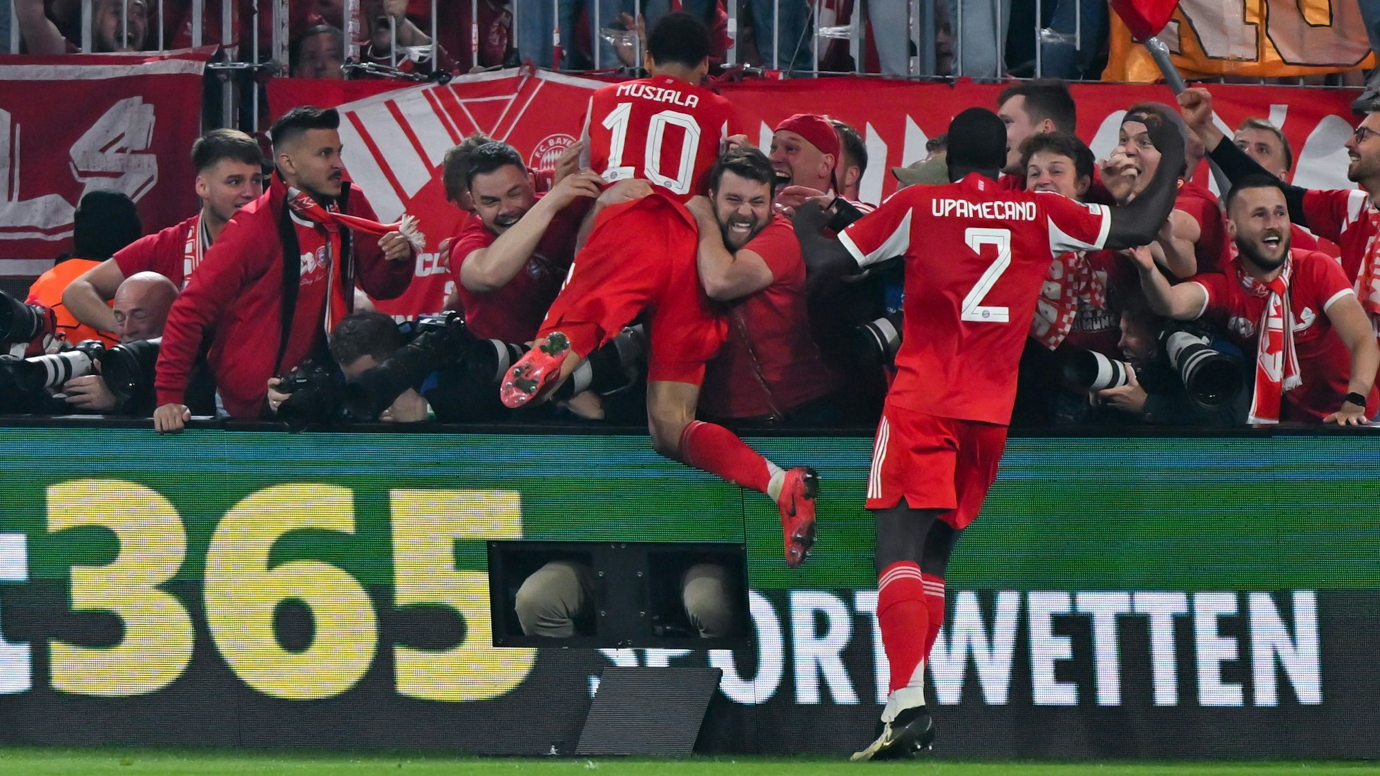 Jamal Musiala (l.) und Dayot Upamecano jubeln beim Spiel gegen Real Madrid mit den Fans.