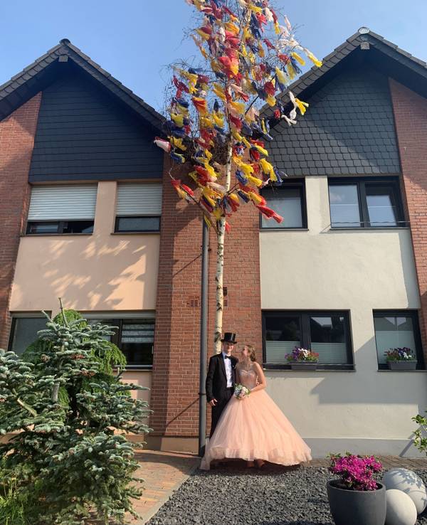 Ein Maibaum mit bunten Bändern steht vor einem Haus