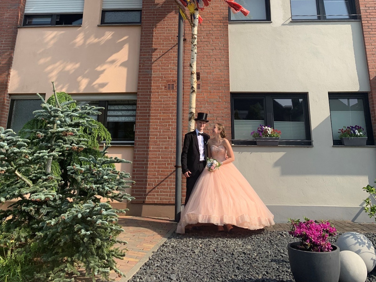 Ein Maibaum mit bunten Bändern steht vor einem Haus