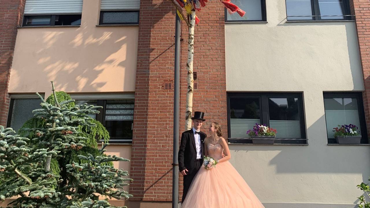 Ein Maibaum mit bunten Bändern steht vor einem Haus