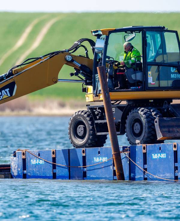 Ein Bagger steht auf einem Steg vor der Insel Poel und legt unter Wasser eine Rinne frei.