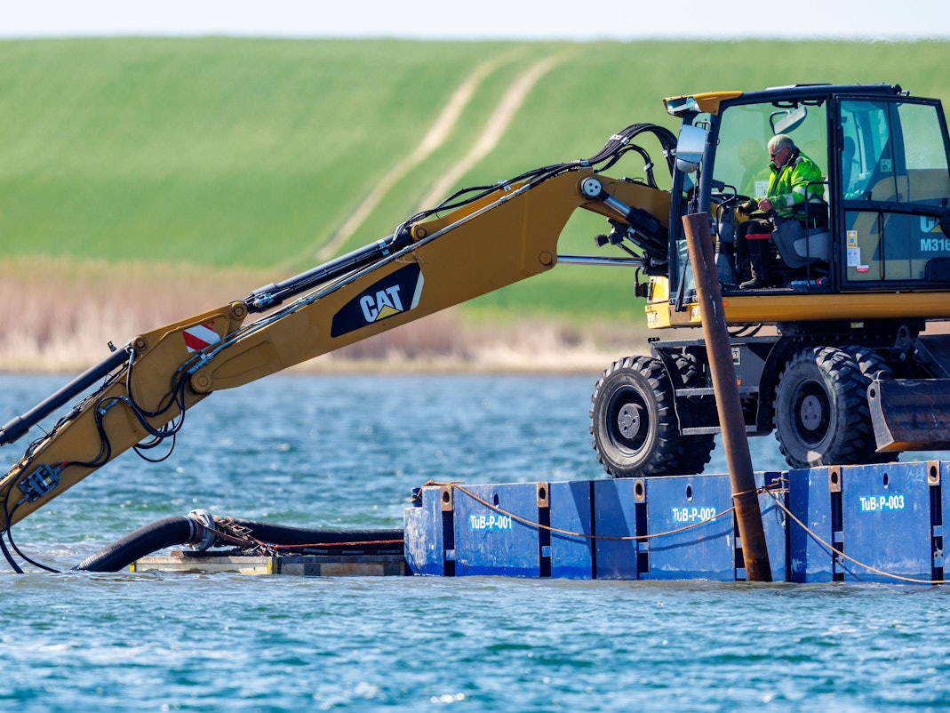 Ein Bagger steht auf einem Steg vor der Insel Poel und legt unter Wasser eine Rinne frei.