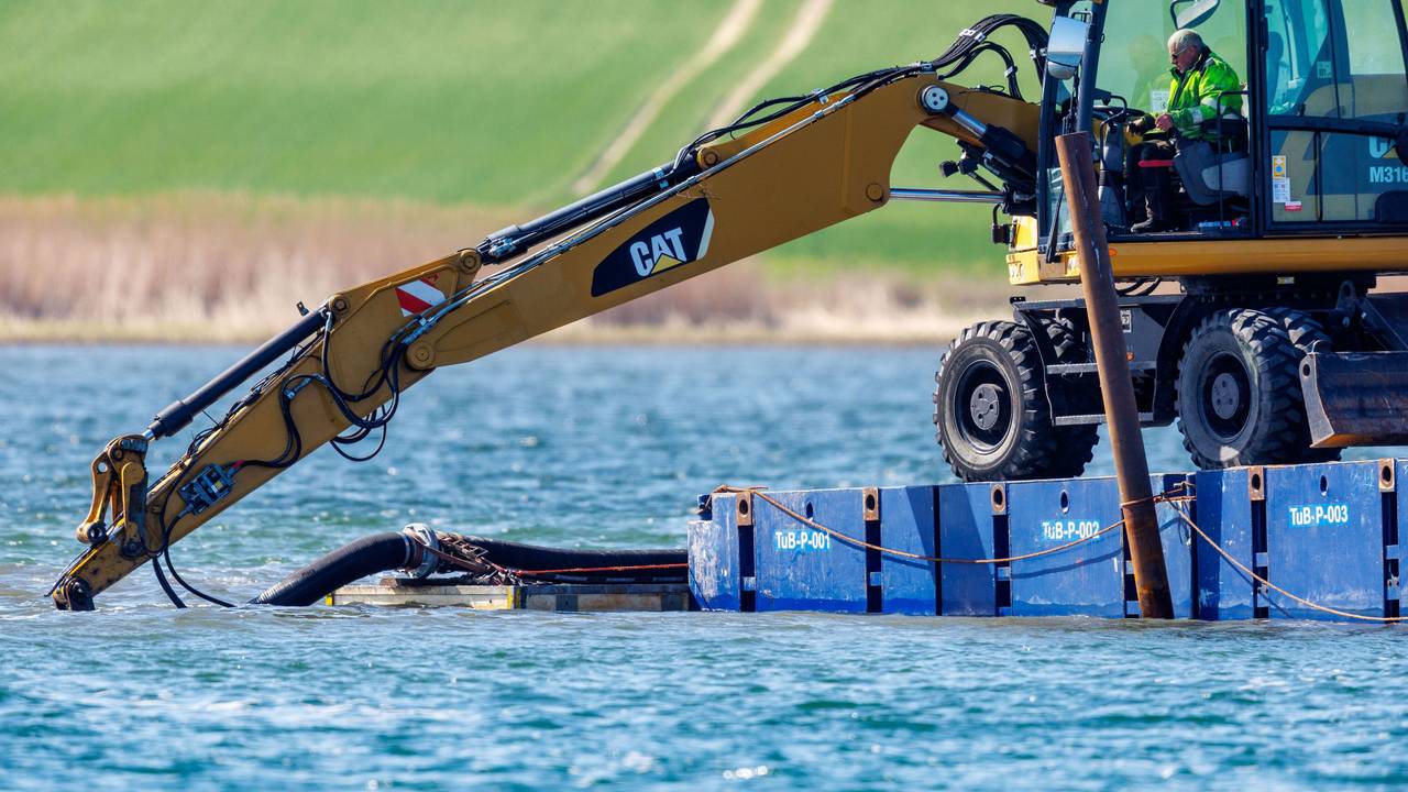Ein Bagger steht auf einem Steg vor der Insel Poel und legt unter Wasser eine Rinne frei.