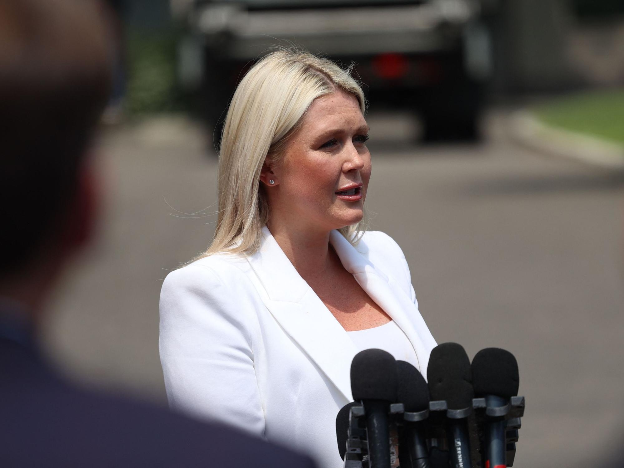 Karoline Leavitt steht auf einer Straße und spricht in mehrere Mikrofone.