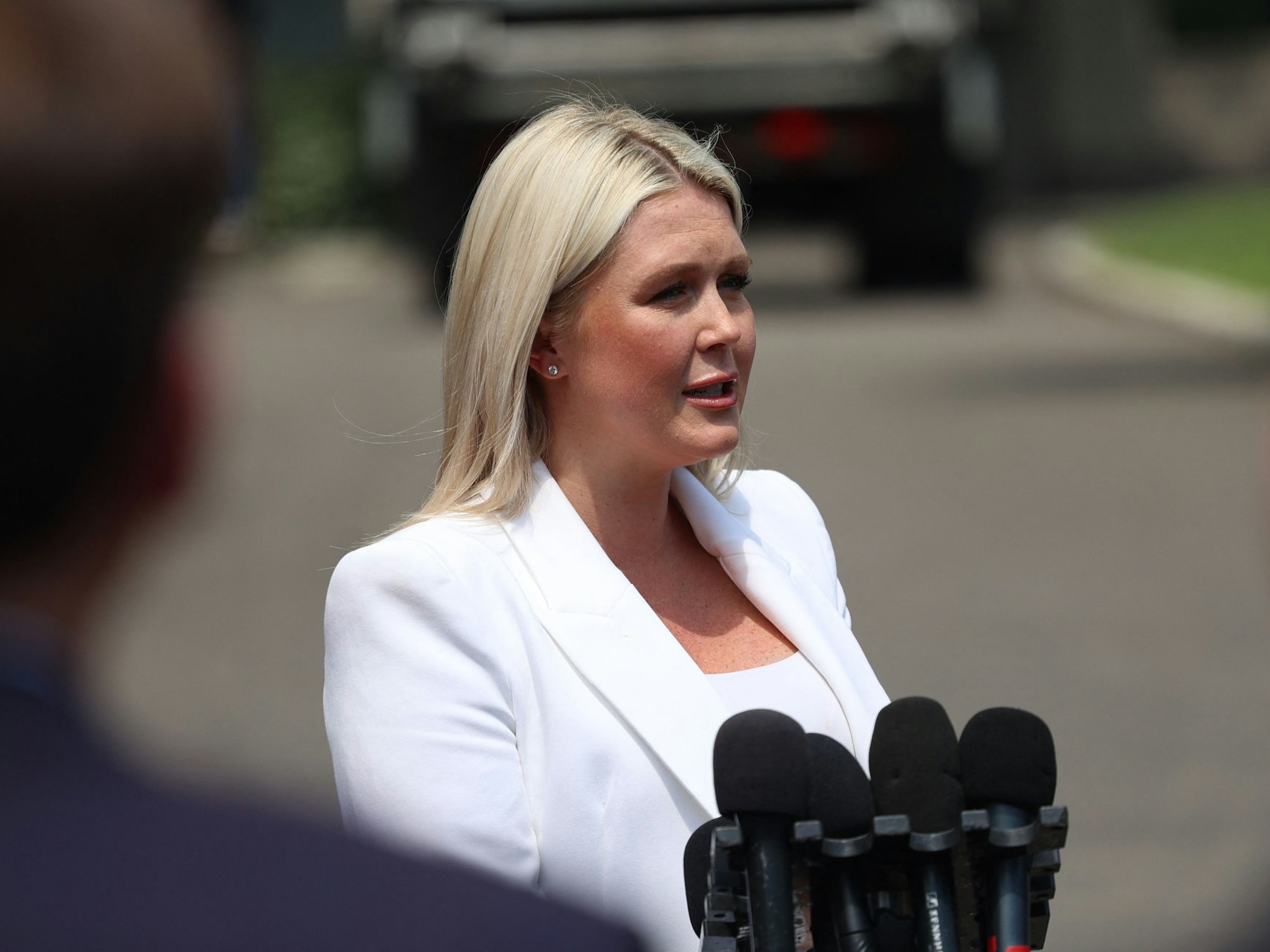 Karoline Leavitt steht auf einer Straße und spricht in mehrere Mikrofone.