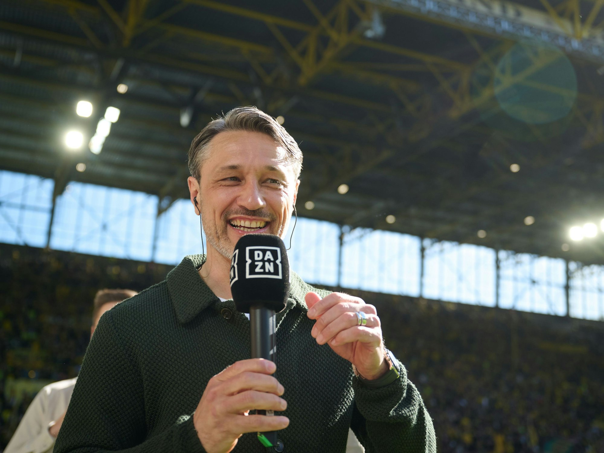 Nico Kovac lacht und hat ein DAZN-Mikrofon in der Hand.