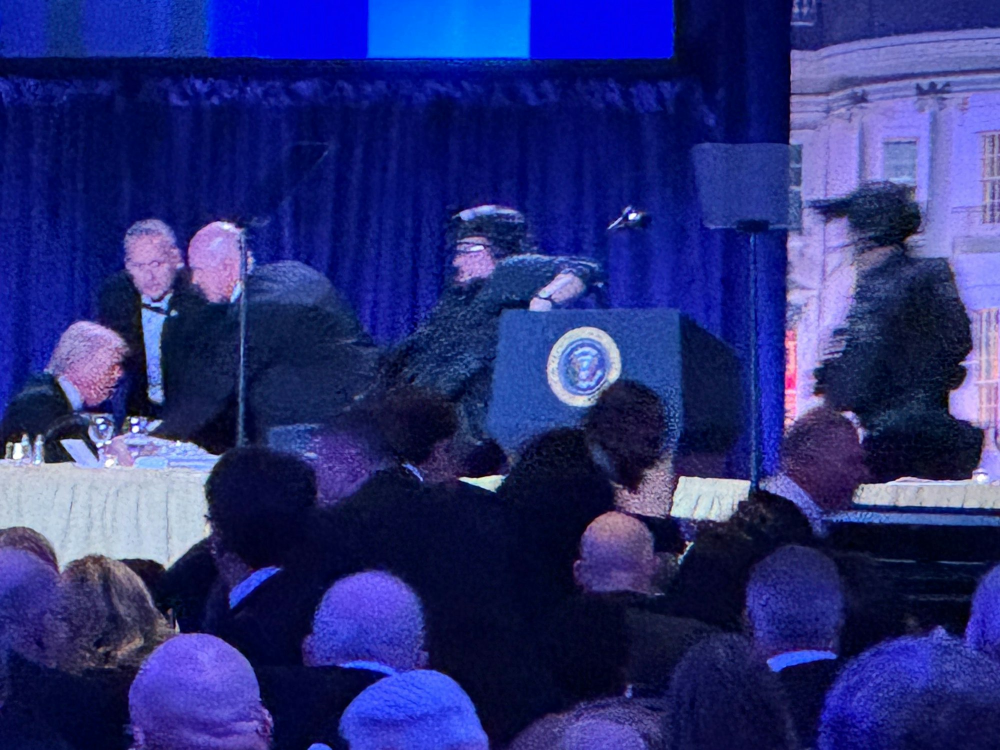 US-Präsident Donald Trump (l) sitzt auf der Bühne, während Agenten des US-Geheimdienstes ihn nach einem Vorfall außerhalb des Ballsaals während des White House Correspondents' Dinner aus dem Ballsaal bringen.