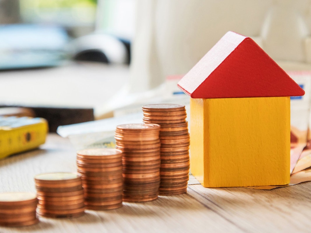 Münzen und ein Haus aus Bausteinen liegen auf einem Tisch