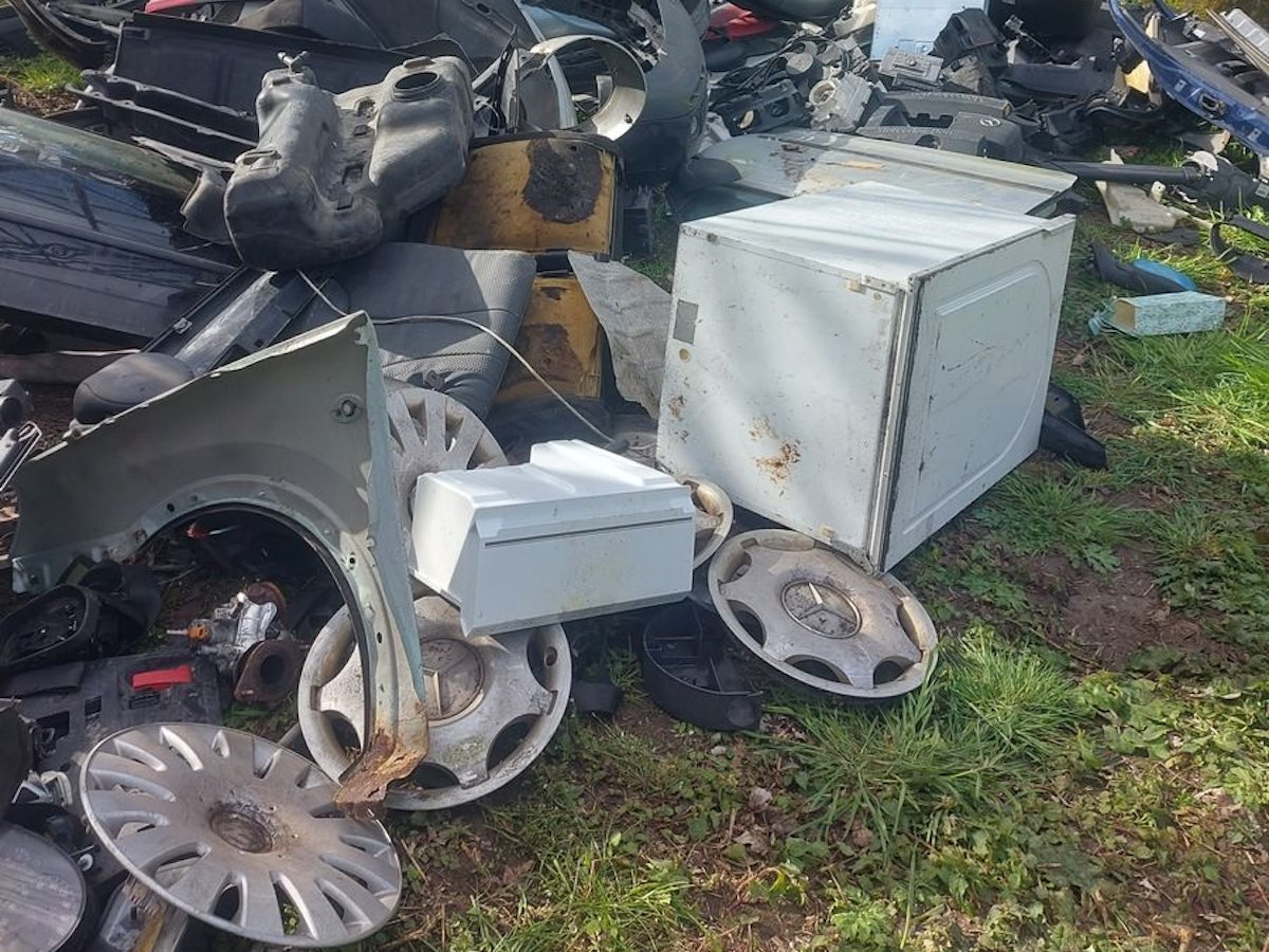 Ein Berg von Müll, darunter Autoteile und Kanister, liegt in einem Waldstück.