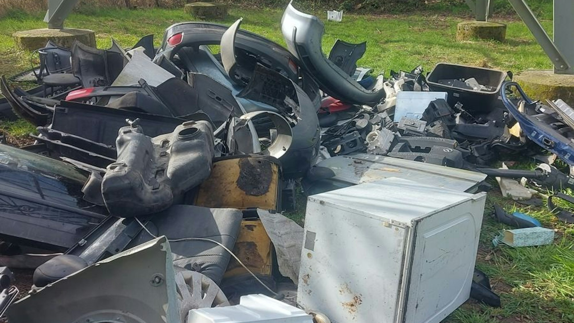 Ein Berg von Müll, darunter Autoteile und Kanister, liegt in einem Waldstück.