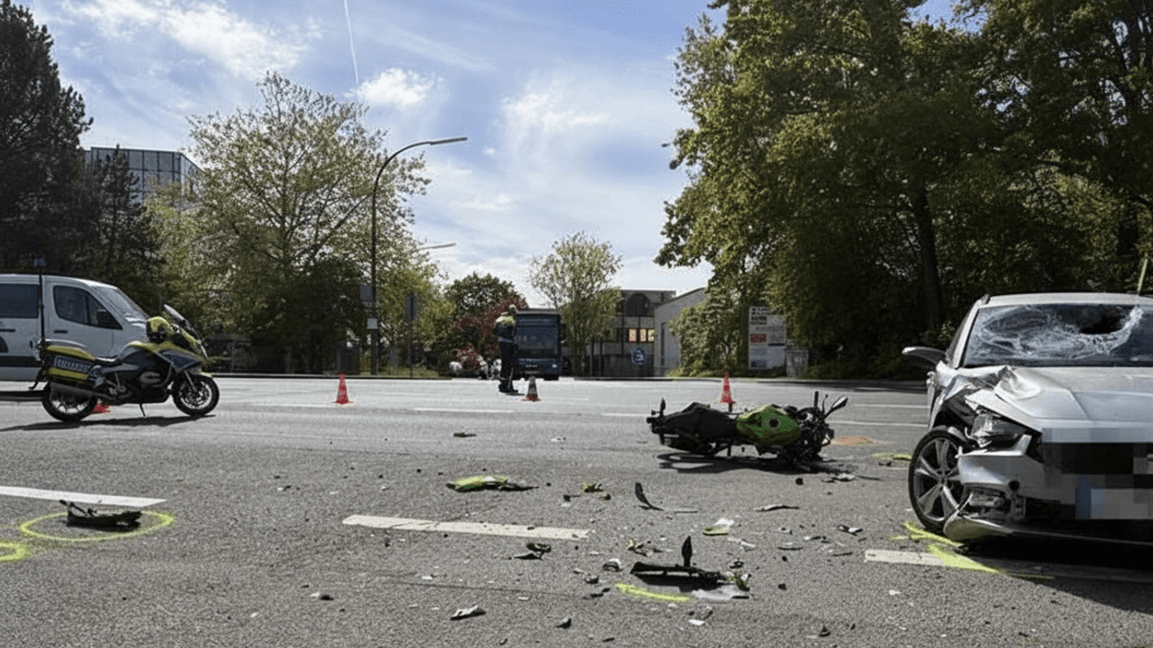 Das Foto zeigt eine Straßenszene nach einem Unfall. Man sieht ein stark beschädigtes Auto auf der rechten Seite und ein Motorrad, das auf der Straße liegt, umgeben von Trümmern.