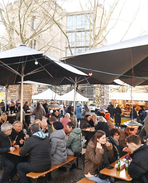 Menschen sitzen auf Bänken unter Sonnenschirmen, essen und trinken.