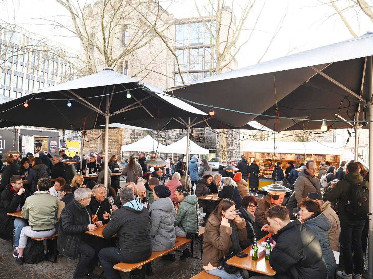 Menschen sitzen auf Bänken unter Sonnenschirmen, essen und trinken.