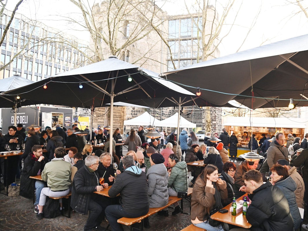 Menschen sitzen auf Bänken unter Sonnenschirmen, essen und trinken.