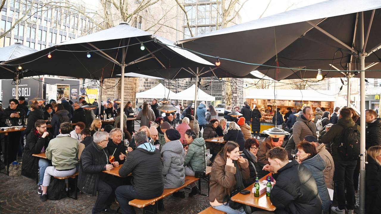 Menschen sitzen auf Bänken unter Sonnenschirmen, essen und trinken.