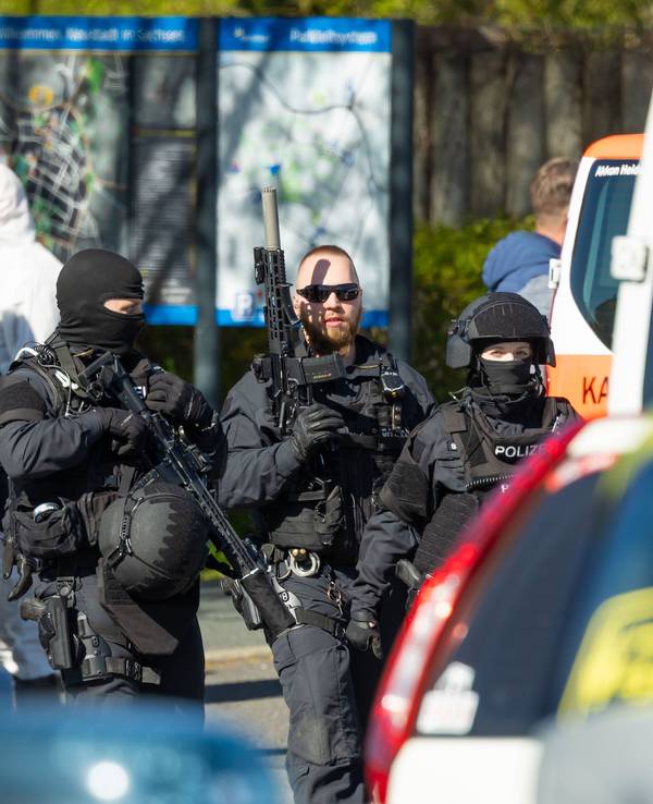 Polizisten und Mitarbeiter der Spurensicherung stehen in der Nähe des Tatortes. Nach Schüssen im Bereich eines Mehrfamilienhauses hat die Polizei zwei Tote und einen Schwerverletzten entdeckt. Die Hintergründe der Tat sind noch unklar.