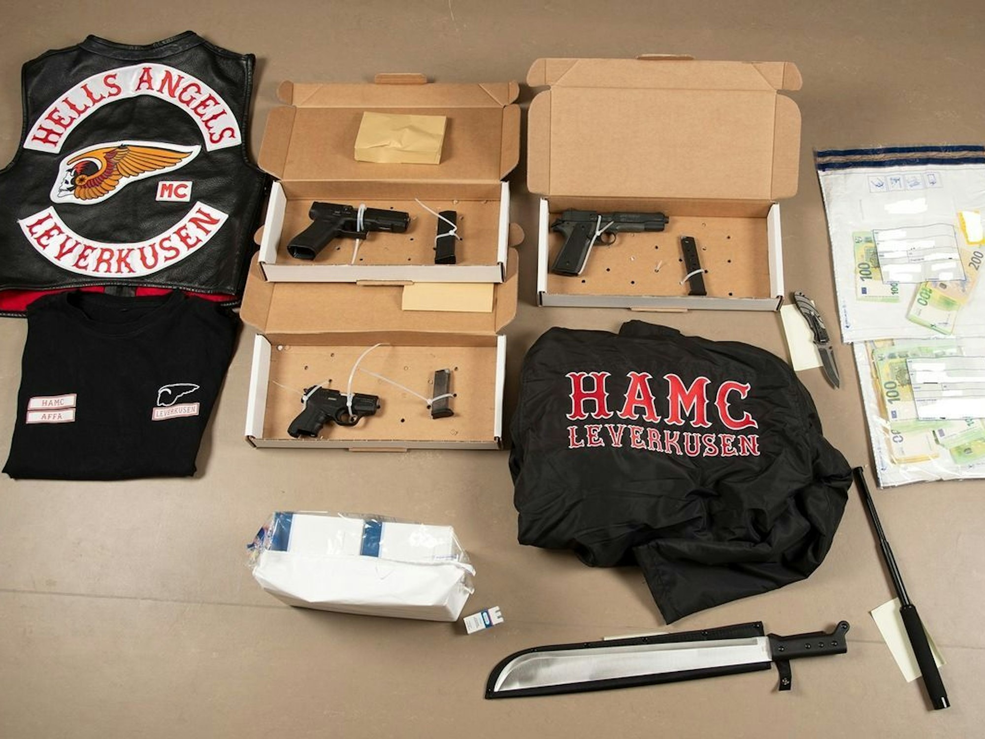 Sichergestellte Gegenstände und Bargeld liegen auf einem Tisch. Bei den Razzien gegen „Hells Angels“-Rocker in Nordrhein-Westfalen haben die Ermittlungsbehörden u.a. Waffen und Vermögenswerte sichergestellt.