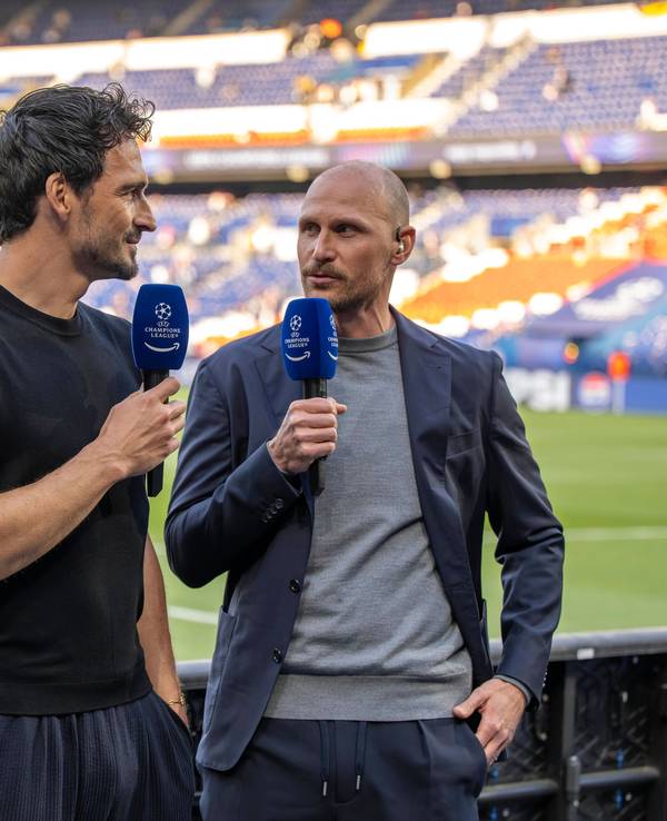 Mats Hummels und Benedikt Höwedes stehen mit Mikrofonen hinter der Bande am Spielfeldrand.