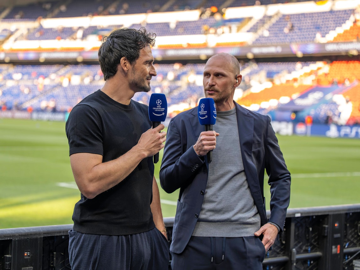 Mats Hummels und Benedikt Höwedes stehen mit Mikrofonen hinter der Bande am Spielfeldrand.