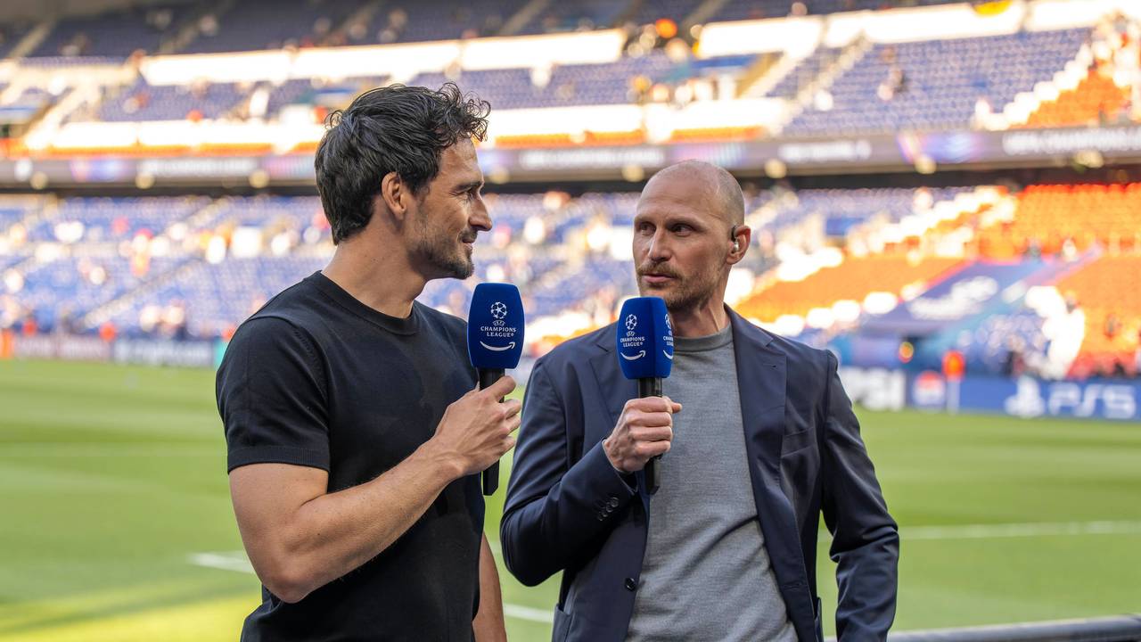 Mats Hummels und Benedikt Höwedes stehen mit Mikrofonen hinter der Bande am Spielfeldrand.