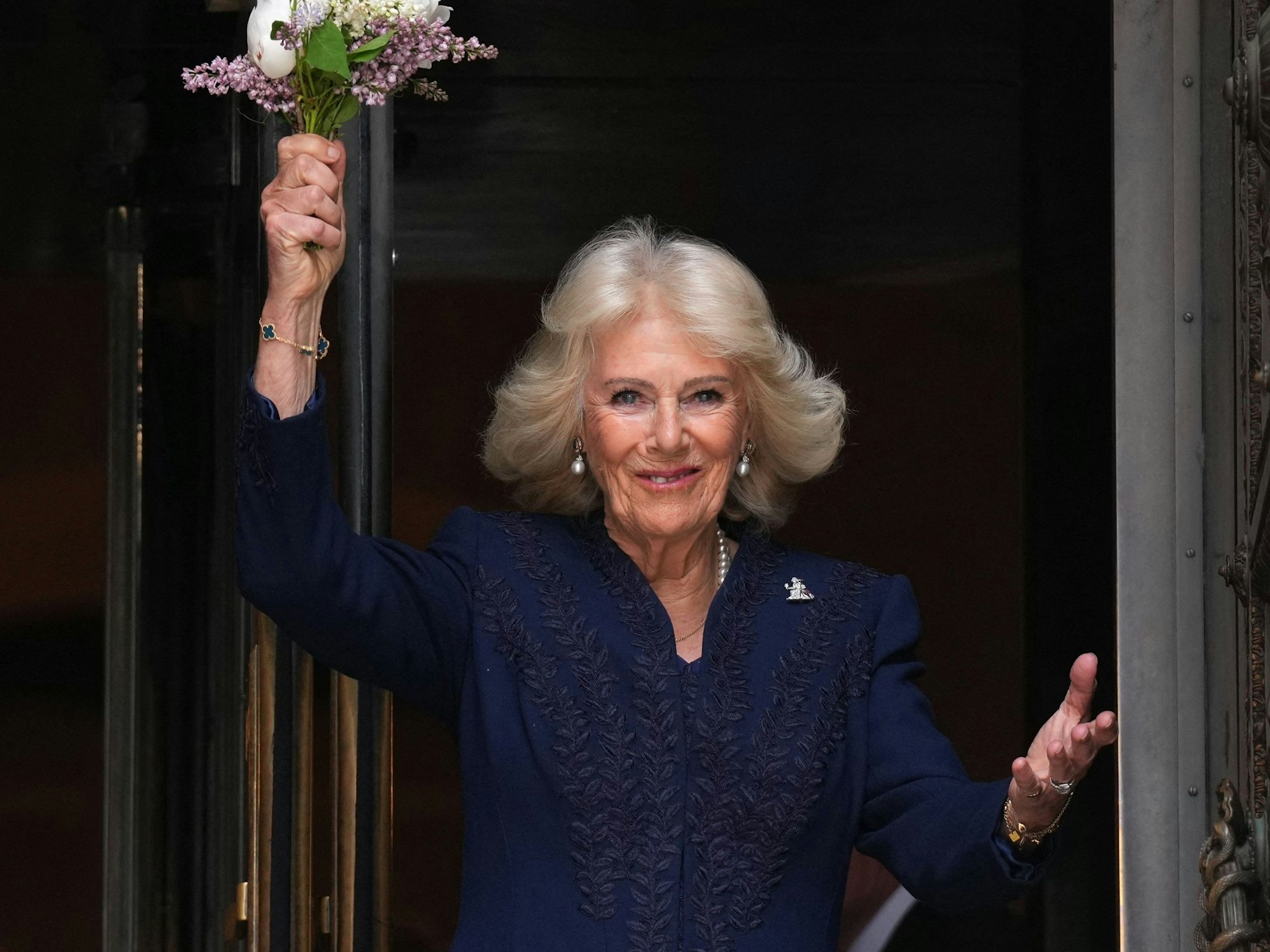 Königin Camilla winkt mit Blumen den Schaulustigen zu.
