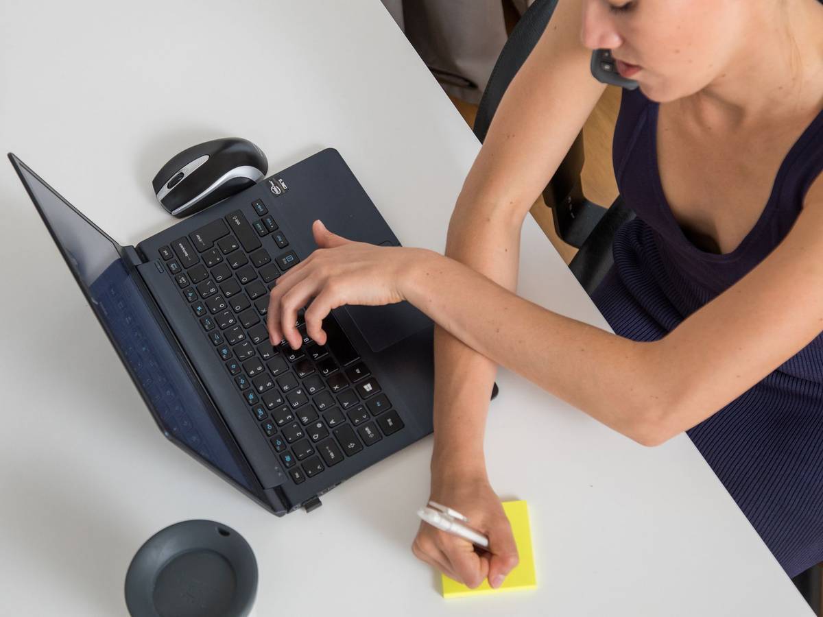 Eine Frau telefoniert, tippt auf Laptop und schreibt Notiz