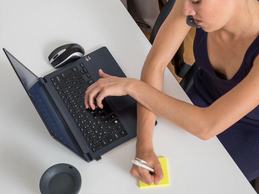 Eine Frau telefoniert, tippt auf Laptop und schreibt Notiz