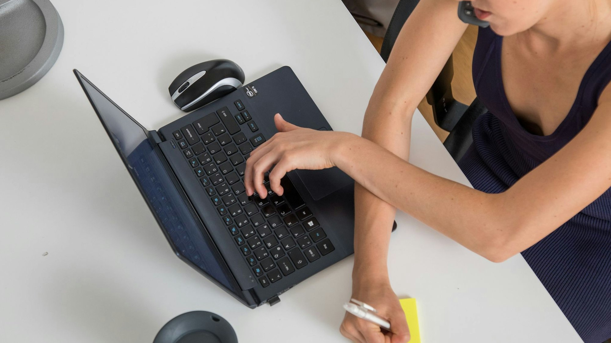Eine Frau telefoniert, tippt auf Laptop und schreibt Notiz