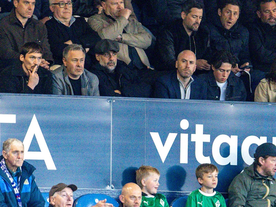 Pep Guardiola mit Mütze auf der Tribüne.