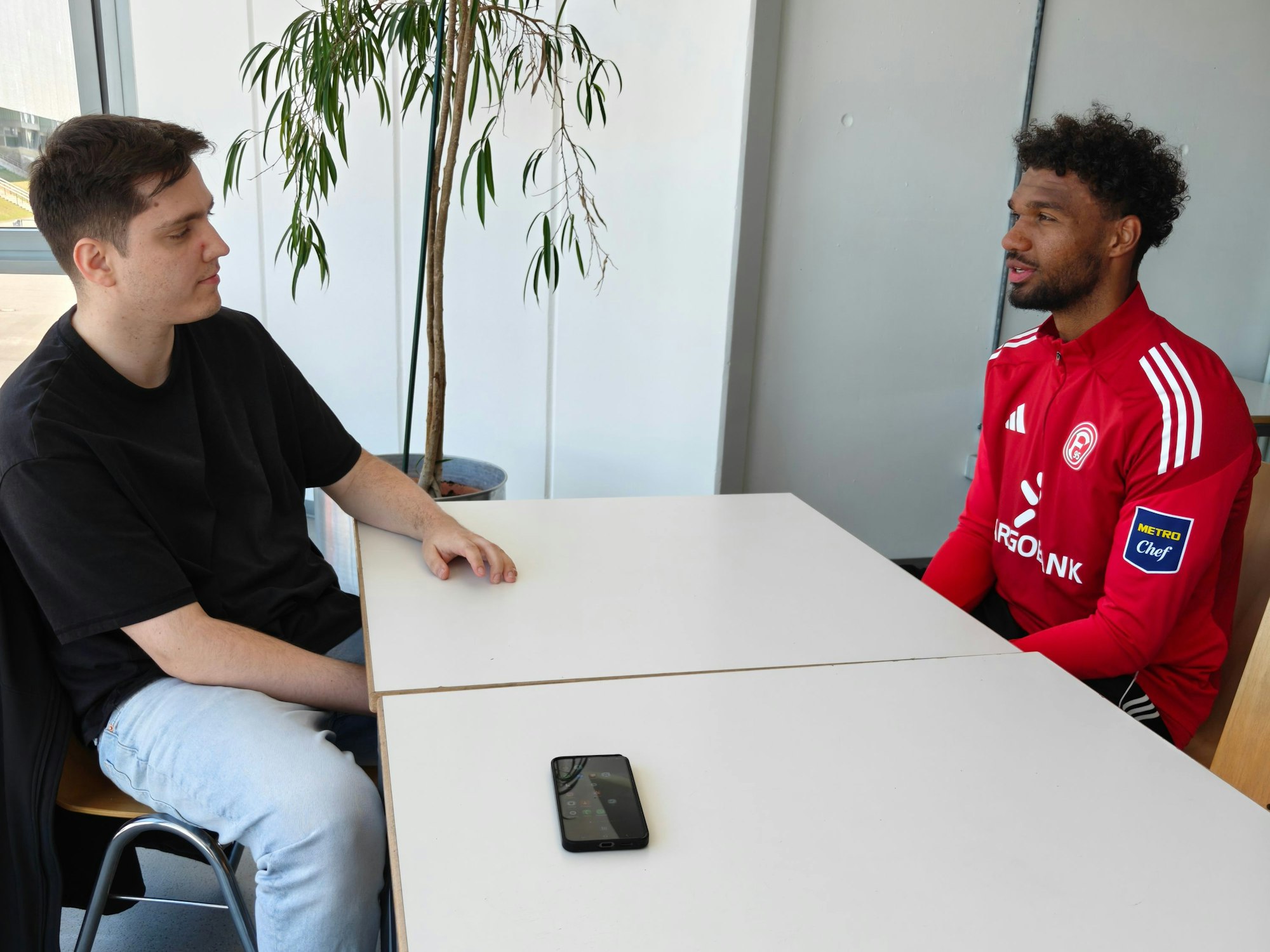 Express-Reporter Sebastian Bucco und Fortuna-Spieler Elias Egouli sitzen an einem Tisch gegenüber und sprechen miteinander.