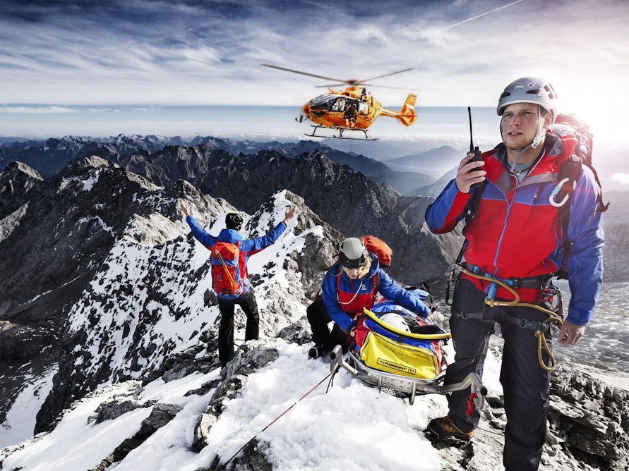 Auch die zweite Staffel der „Bergretter im Einsatz“ zeigt Bergwachteinsätze in den bayerischen Alpen - hautnah und in beeindruckenden Bildern. Drei Angehörige der Bergwacht, die sich mit einer geretteten Person auf einem Berggipfel befinden, weisen einen anfliegenden Hubschrauber ein. (Bild: BR / Timeline Production)