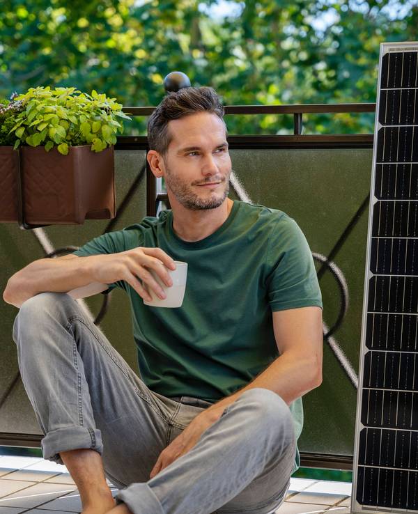 Mann mit Kaffee, Solarmodul und Pflanzen auf Balkon