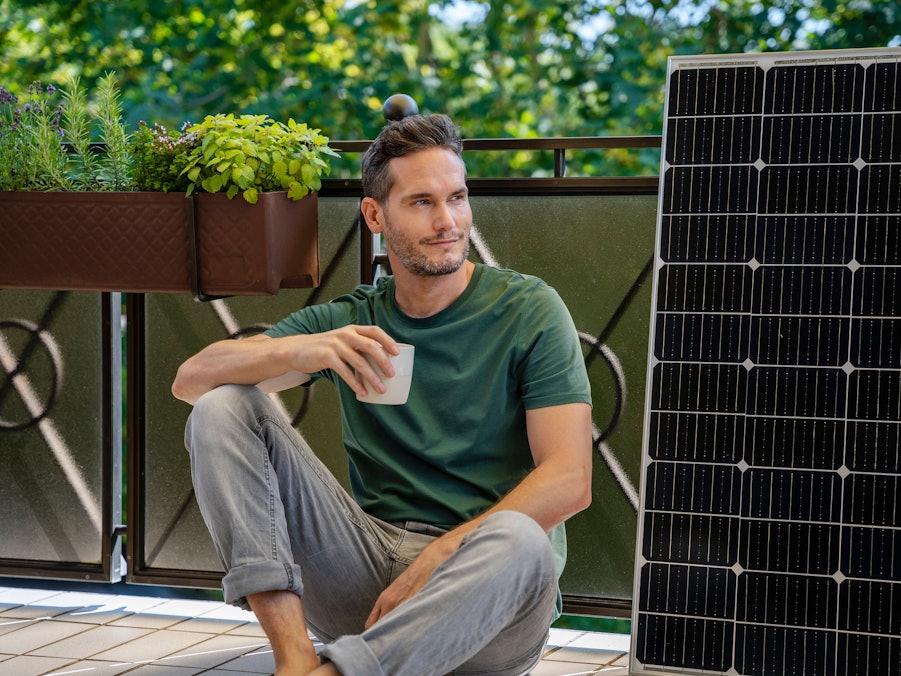 Mann mit Kaffee, Solarmodul und Pflanzen auf Balkon